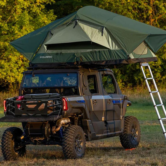 Camouflage truck with a green rooftop tent in a natural setting